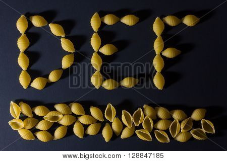 English alphabet in the form of pasta shells , laid out on a dark background .