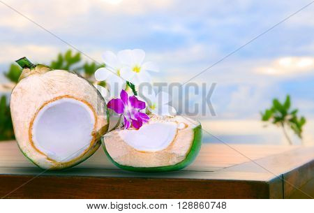 twon half of green coconut water on top wood table with tropical orchid flowers and white frangipani bouquet decorated