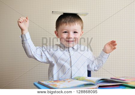 Young schoolboy playing with books and smiling as he sits at his desk in classroom.