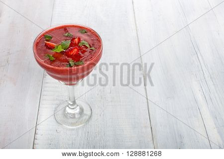 A glass of strawberry smoothie on a whight wooden background