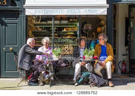 KINGS CROSS, LONDON, UK - MAY 5, 2016. Two elderly couples taking a break from sightseeing and sitting at the outdoor tables of a small French cafe on the streets of London.