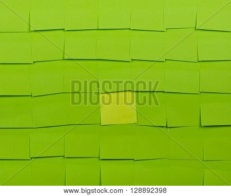 Background of green sticky notes. Yellow sticky note is among green sticky notes.