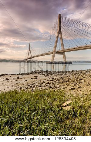 View of the International Bridge over the Guadiana river a cloudy day at sunset with a large rock in the foreground. Spain-Portugal border. Picture taken from the Spanish shore.