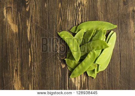 Green peas pods over wooden table. Top view