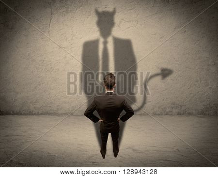 An experienced tricky businessman in suit looking at his devil desguise shadow reflected on the wall concept