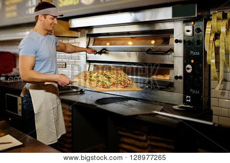 Handsome pizzaiolo making pizza at kitchen in pizzeria.
