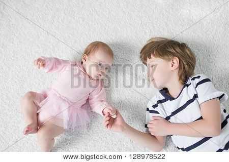 Brother Toddler with baby sister lying on the floor in the nursery.