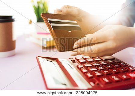 Woman Is Holding Purse, Credit Card In Hands And Calculating The Costs. Pink Table. Flowers On The T