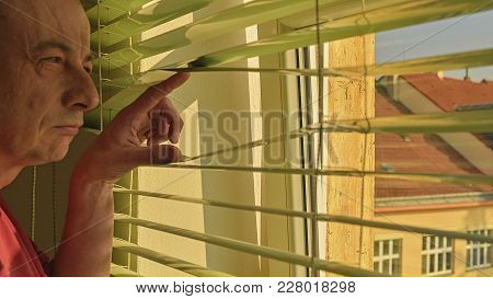 Midlle Age Man Looking Through A Jalousie. Themes Curiousity, Surveillance Or Eyesight.