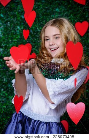 Happy pre-teen girl poses surrounded by little hearts over lawny background. First love. Valentine's Day.