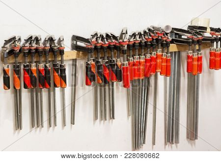 woodworking, construction and work tool concept - one-handed bar clamps hanging on wall