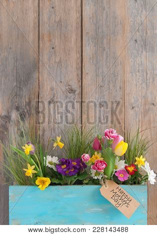 Mothers Day Gift Label Attached To A Selection Of Spring Flowers Inside A Wooden Plant Holder