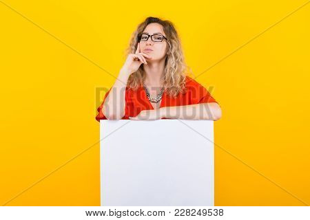 Portrait Of Attractive Thoughtful Curly-haired Woman In Red Dress And Eyeglasses Isolated On Orange 