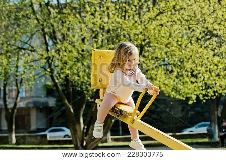 Balance, Equilibrium, Harmony. Girl Sit On Seesaw On Sunny Day. Kid On Teeter Totter Outdoor. Child 