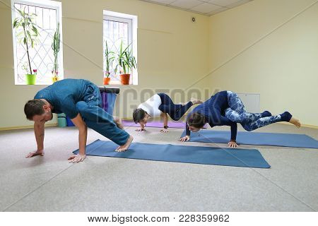 Two Women And Men Of American Appearance Engaged In Yoga, People Sit On Floor On Fitness Rugs And Pe
