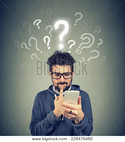Young Man Having Questions While Using Contemporary Device In Puzzlement.