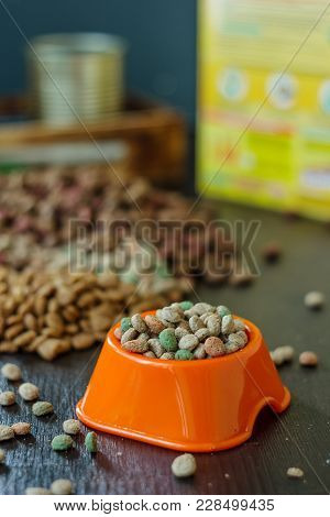 Plastic Bowl With Dry Pet Food On Black Wooden Board