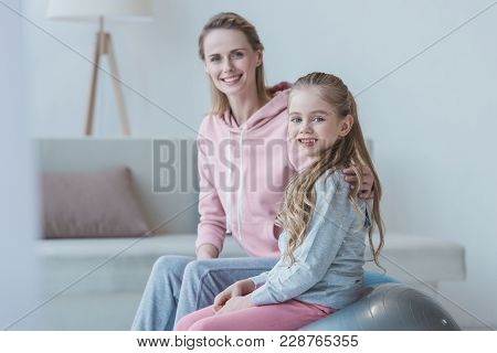 Mother And Daughter Loooking At Camera At Home While Child Sitting  On Fit Ball