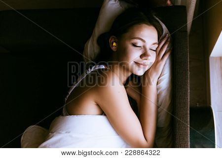 A Woman Sleeps In Bed Under A Blanket With Earplugs In The Ears