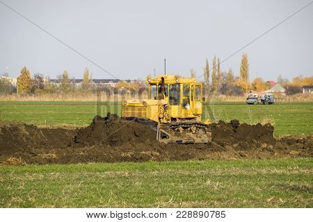 The Yellow Tractor With Attached Grederom Makes Ground Leveling. Work On The Drainage System In The 