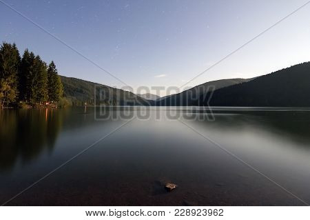 Stars In The Night Sky And Carpathian Mountains Reflecting In A Lake At Nigh. Bright Moon Light In T