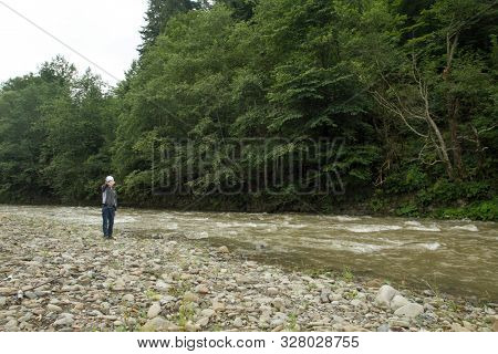 Boy near the river is dropping stones in the water. Boy have fun