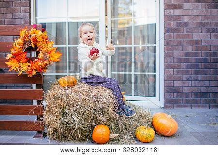 Adorable Laughing Caucasian Baby Toddler In White Knittes Jacket Sitting On The Haystack With Pumpki