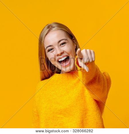 Bullying Concept. Young Girl Laughing At Someone And Pointing Finger To Camera, Orange Studio Backgr