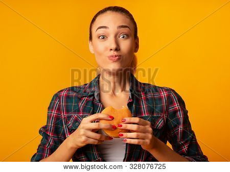Slim Girl Eating Burger Having Cheat Meal Day Standing On Yellow Studio Background. Unhealthy Diet