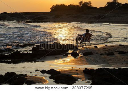 A Man Sitting In An Armchair And Admiring The Sunset. The Concept Of Happiness, Relaxation, Vacation