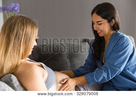 Midwife Visiting Expectant Mother. Young Woman Touching Belly Of Pregnant Patient Lying On Couch. Pr