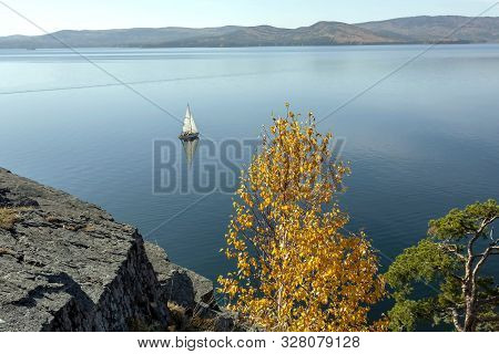 Sailing Boat On The Calm Lake Turgoyak, View From The Rocky Shore In Autumn, Southern Urals