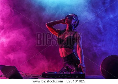 Young Sexy Woman Dj In Bra And Sunglasses Playing Music. Headphones And Dj Mixer On Table. Colorful 
