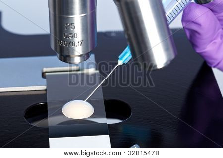 Photo of a sperm sample on a microscope slide with a syringe being used to extract an embryology specimen for analysis.