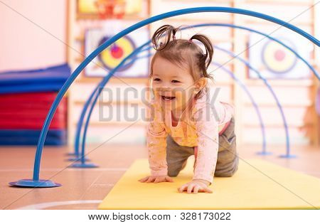 Baby Toddler Crawling On Floor Through Tonnel In Gym Class. Lifestyle Concept Of Children Active Gam