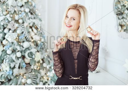 Cute Blonde Woman Near A Christmas Tree Holds Bitcoins In Her Hands And Laughs.