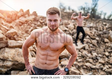 Two Fitness Strongmen Having Workout Outdoor In A Rocky Background. Bodybuilders Concept Background 