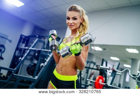 Gorgeous Blonde Woman Is Warming Up With Dumbbells And Doing Workout At A Gym Looking From Her Back.