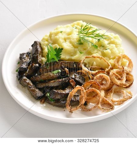 Close Up Of Roasted Beef Liver With Mashed Potatoes And Fried Onion Rings On White Plate Over Stone 