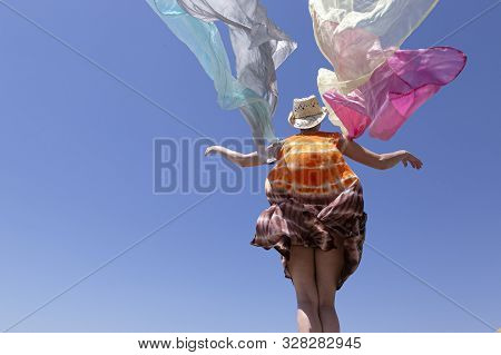 Woman In Straw Hat With Many Colored Scarves With Arms Stretched In The Wind