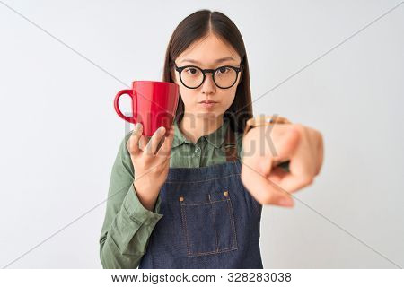 Chinese barista woman wearing apron glasses drinking coffee over isolated white background pointing with finger to the camera and to you, hand sign, positive and confident gesture from the front