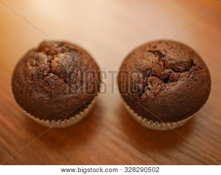 Two Chocolate Muffins On The Brown Wooden Table.