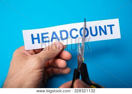 Person Cutting Headcount Using Scissors On Blue Background