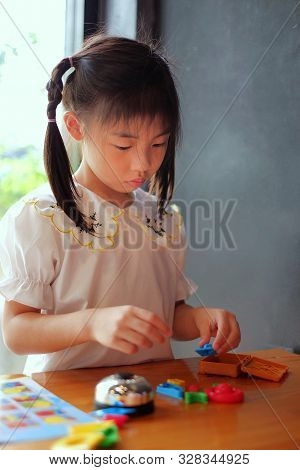 A Cute Asian Girl Playing With Colorful Plastic Toys From A Board Game On A Wooden Table.