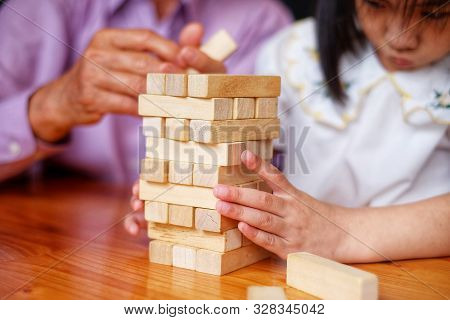 An Grandfather Is Teaching His Granddaughter To Play A Block Wood Tower Game.