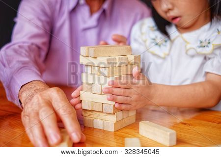 An Grandfather Is Teaching His Granddaughter To Play A Block Wood Tower Game.