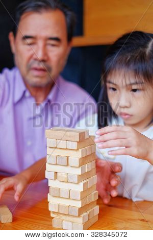 An Grandfather Is Teaching His Granddaughter To Play A Block Wood Tower Game.