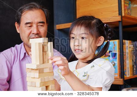 An Grandfather Is Teaching His Granddaughter To Play A Block Wood Tower Game.