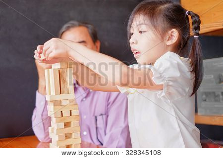 An Grandfather Is Teaching His Granddaughter To Play A Block Wood Tower Game.