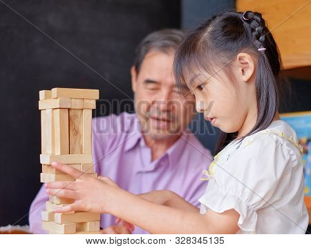 An Grandfather Is Teaching His Granddaughter To Play A Block Wood Tower Game.